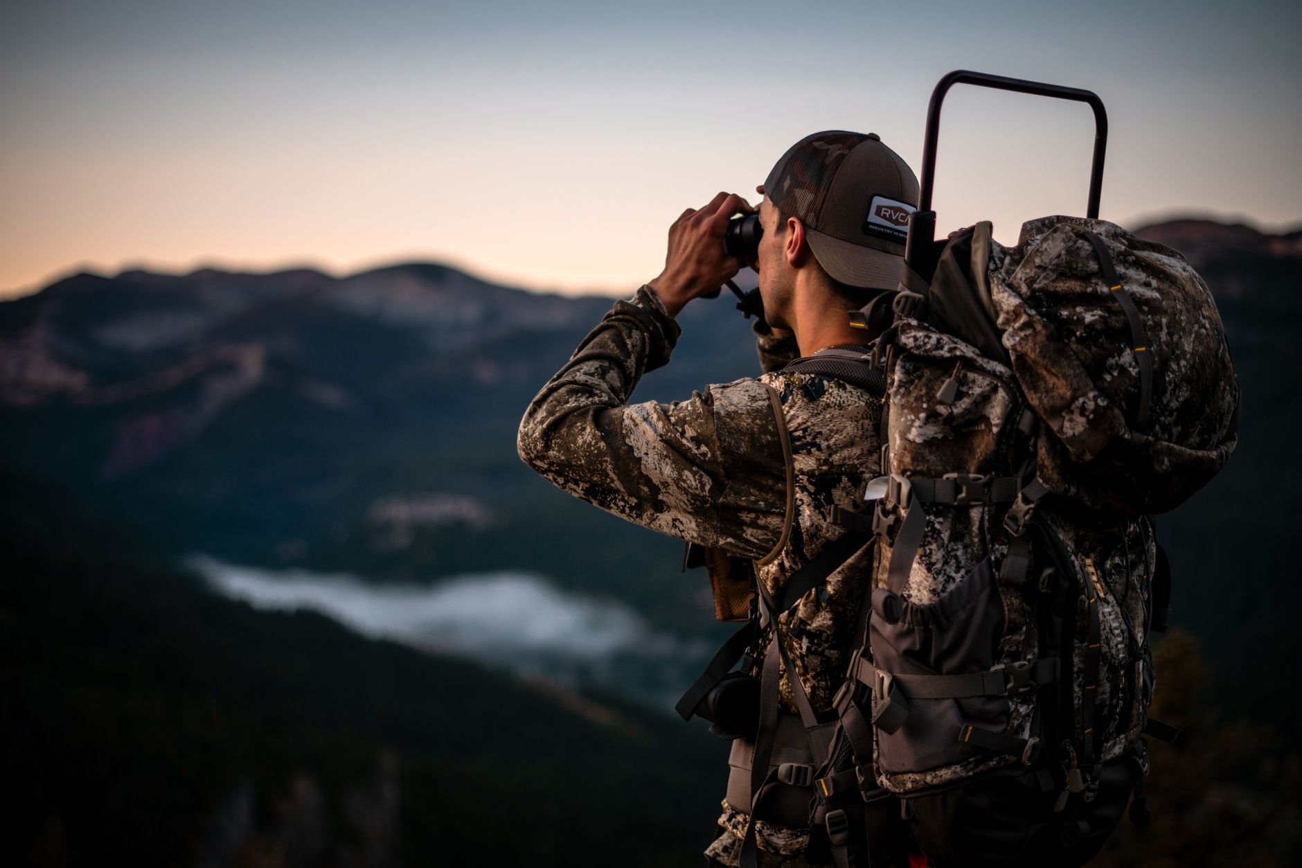 Hunter using a spotting scope from a rocky vantage point in high mountain terrain